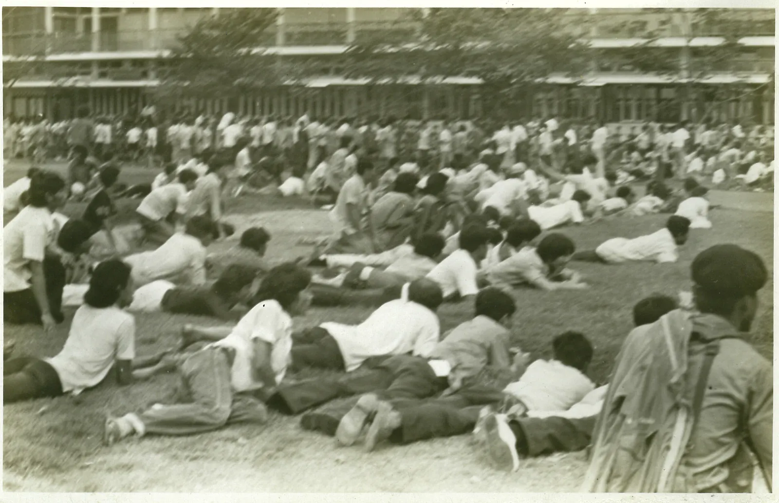 Students in shirts and trousers lie and crawl across the grass of the football field.