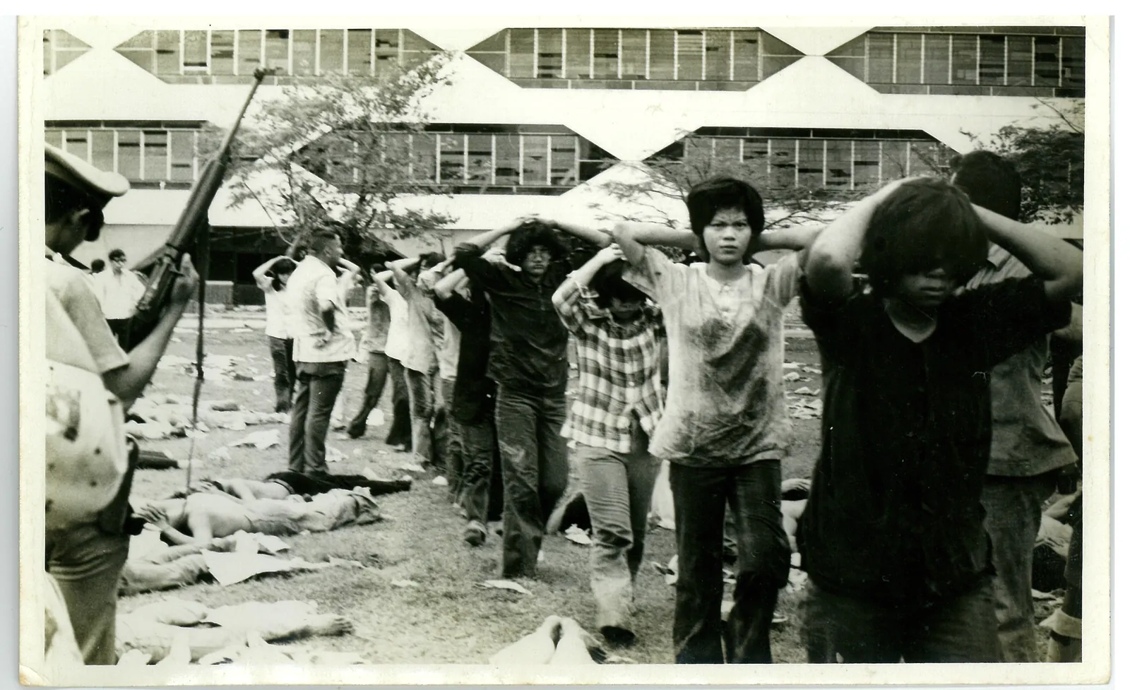 Young people walk in a line with their hands on their heads past an armed man on the Thammasat football field.