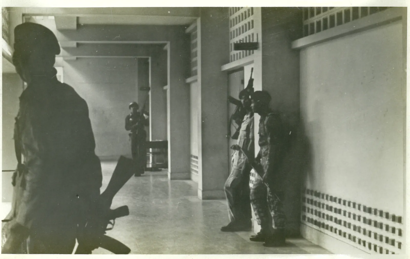 Armed men stand in the shadows of a corridor inside a university building.